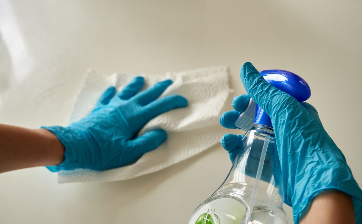 Mains gantées désinfectant une surface avec un spray et un essuie-tout