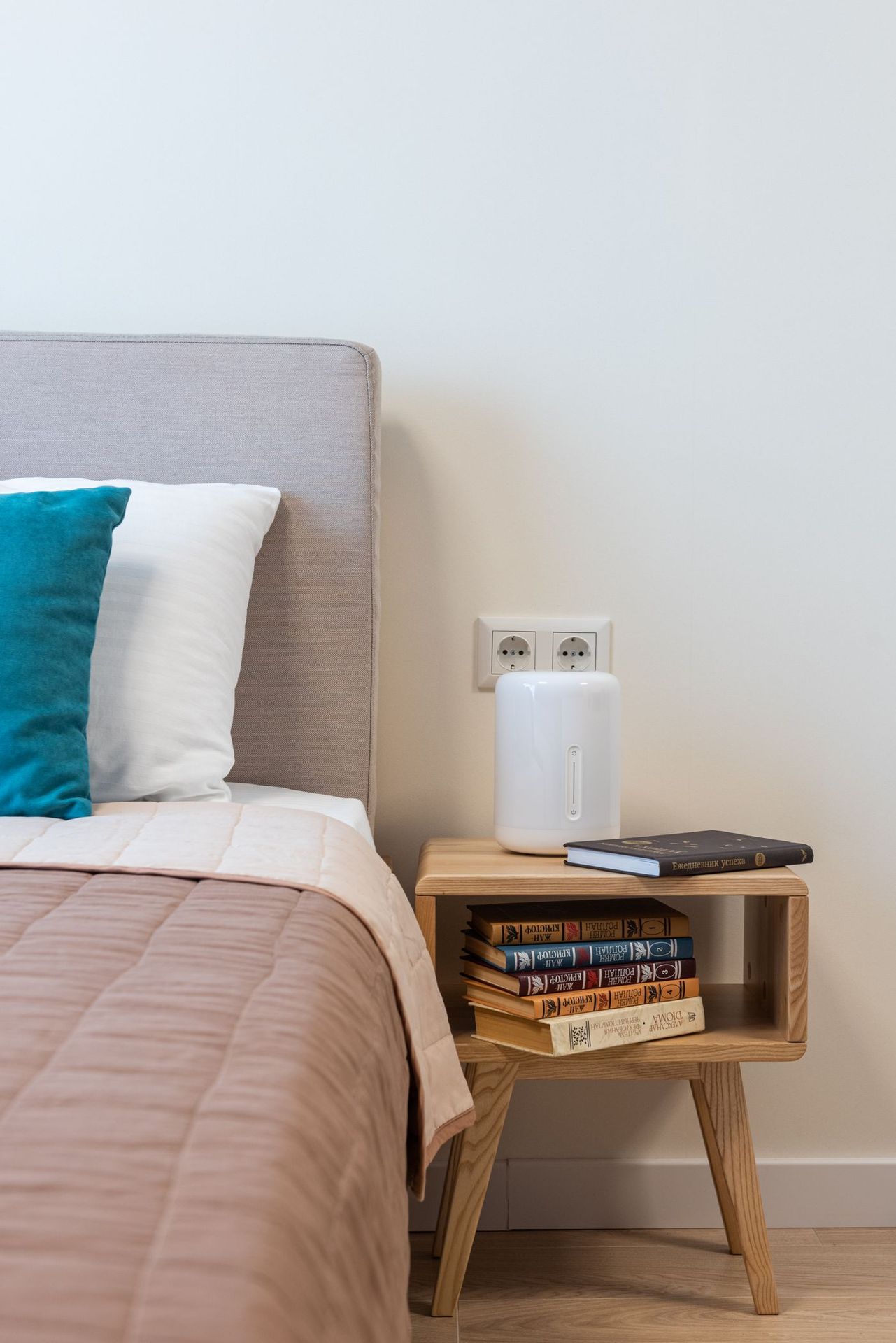 Humidificateur blanc posé sur une table de nuit en bois à côté d'un lit, dans une chambre claire